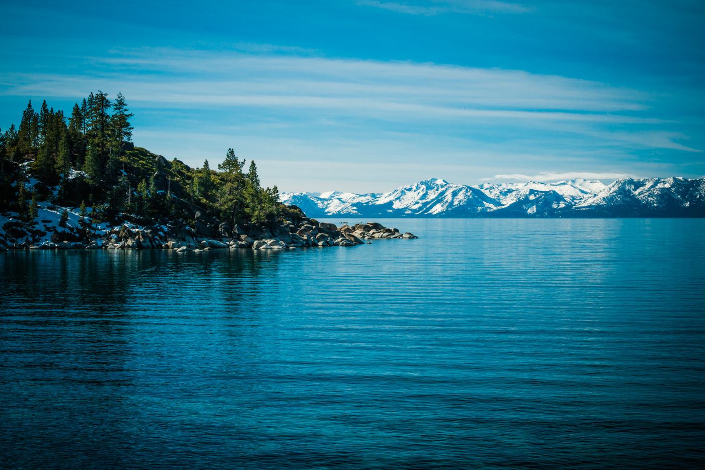 Lake Tahoe on a still day, with pines on the shore and snow on the far mountains